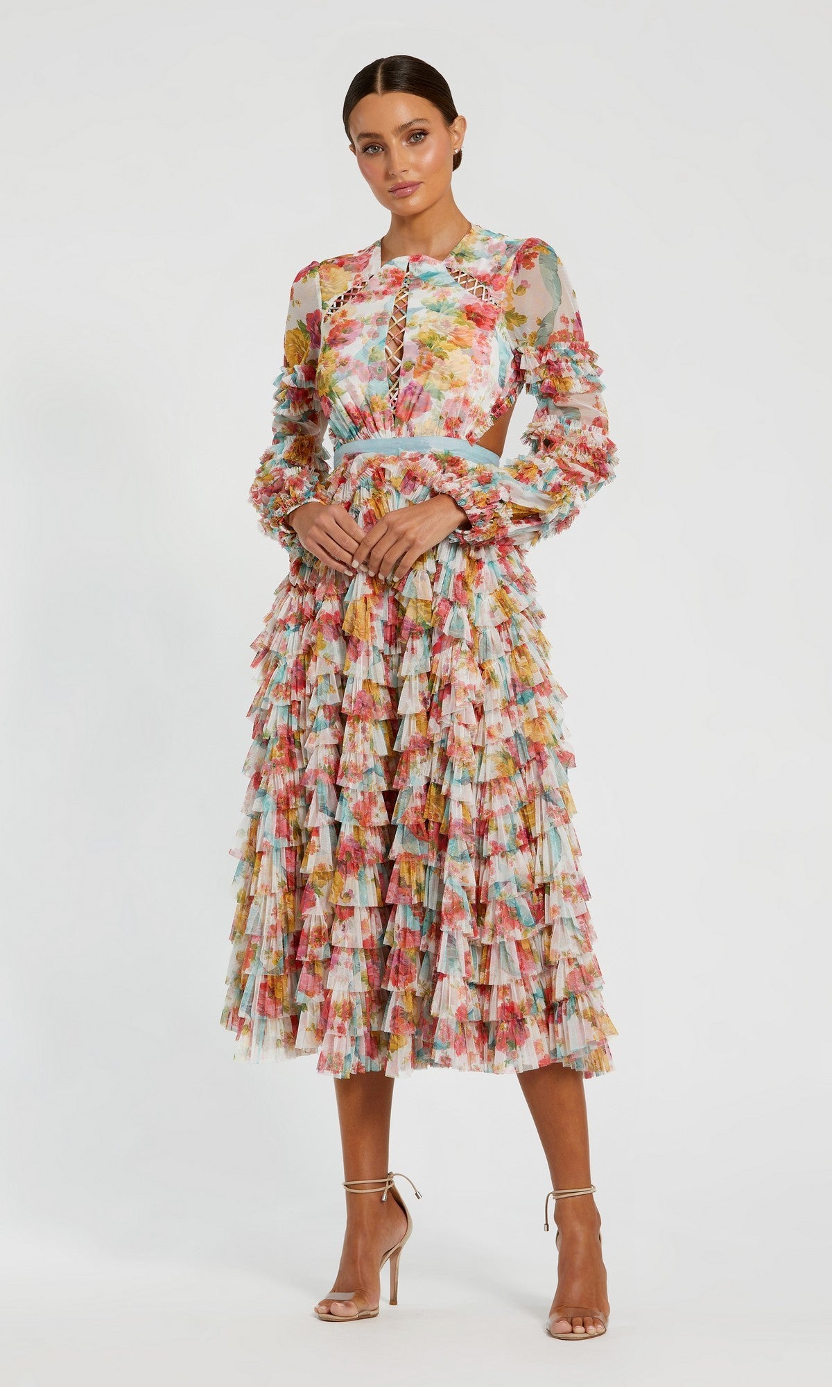 A woman stands elegantly against a plain background in the Mac Duggal 8130 Midi Wedding Guest Dress in White Multi, featuring vibrant floral mesh, ruffled layers, and paired with nude high-heeled sandals.